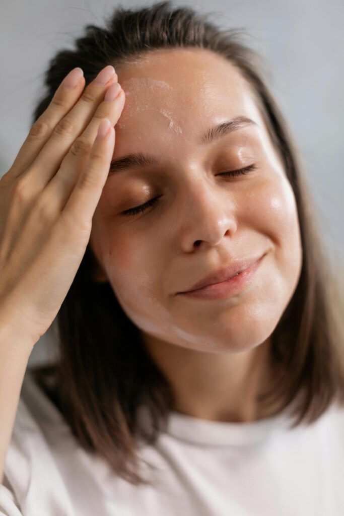 Close-up of a young woman happily applying skincare cream, enjoying a moment of self-care.